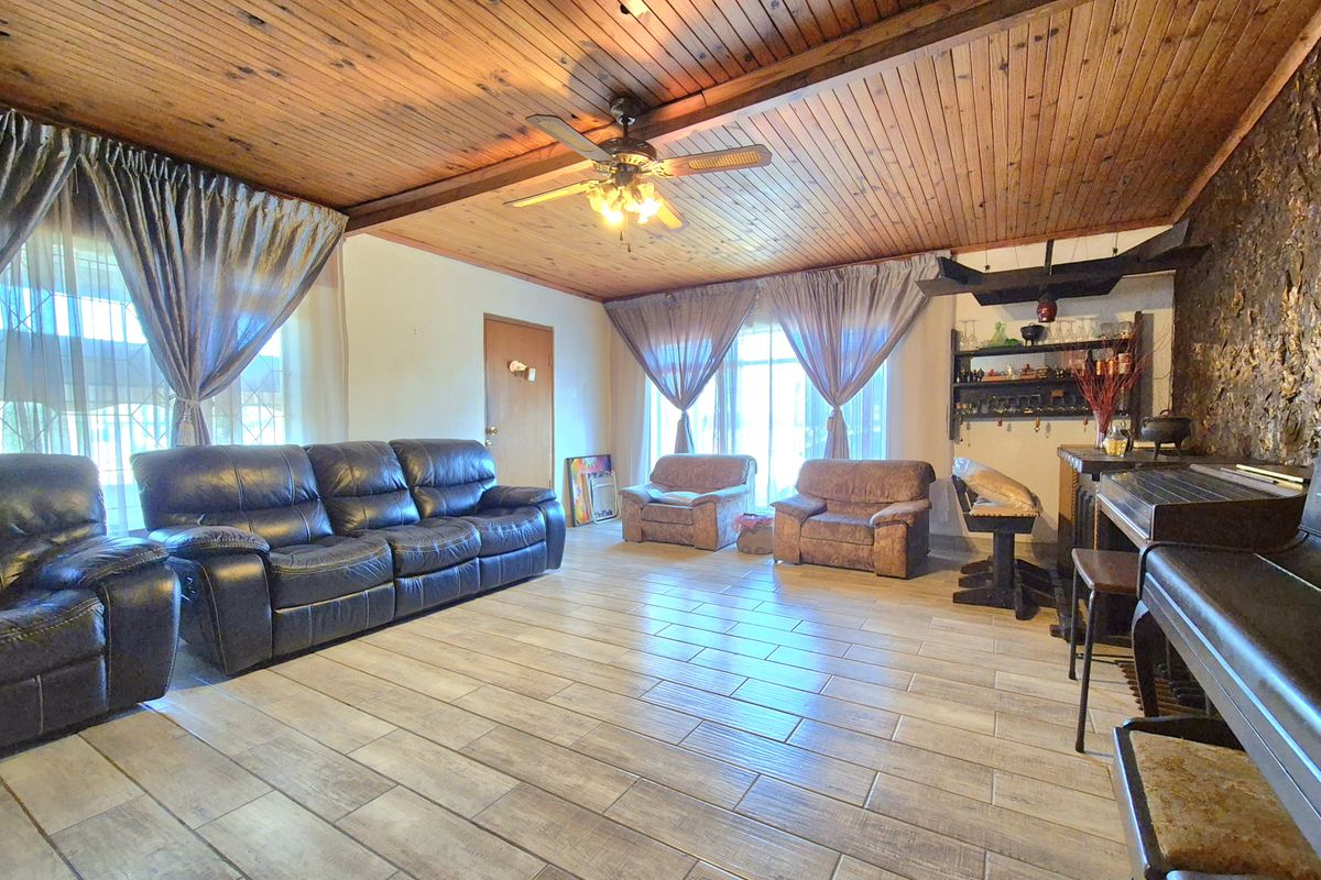 Spacious living room featuring a timber-clad ceiling with exposed beams, a stone feature wall, and durable tiled flooring.