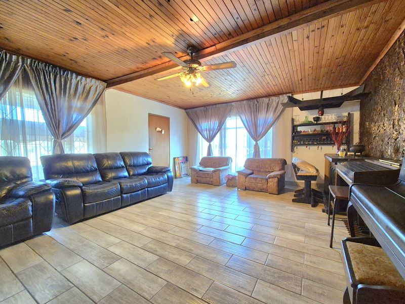 Spacious living room featuring a timber-clad ceiling with exposed beams, a stone feature wall, and durable tiled flooring.