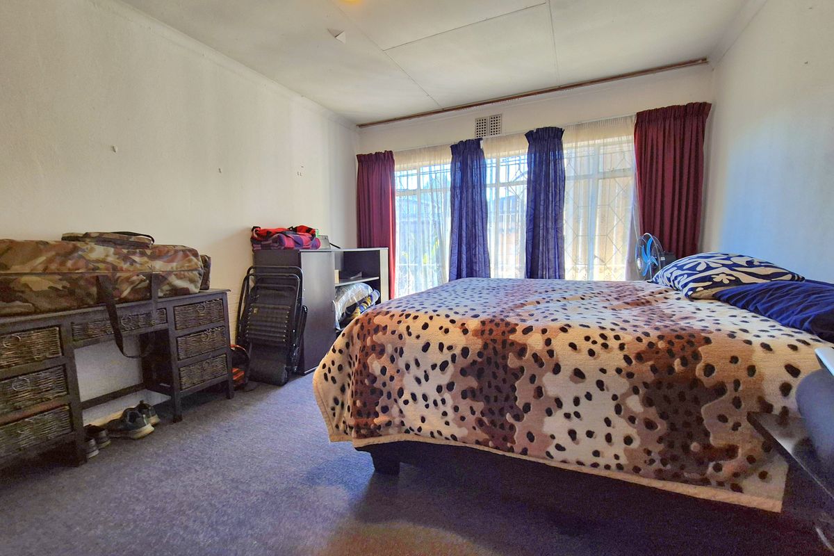 A bedroom featuring a ceiling fan and large windows with security bars, requiring cosmetic updates to the ceiling and wall finishes.
