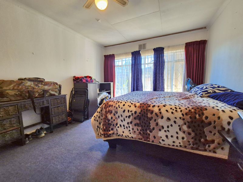 A bedroom featuring a ceiling fan and large windows with security bars, requiring cosmetic updates to the ceiling and wall finishes.