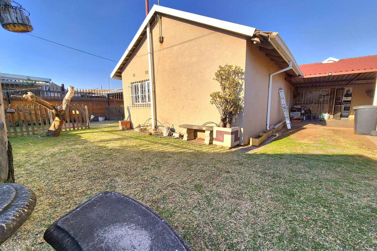 Rear view of the property showing the garden area, exterior wall with security bars, and an attached carport structure.
