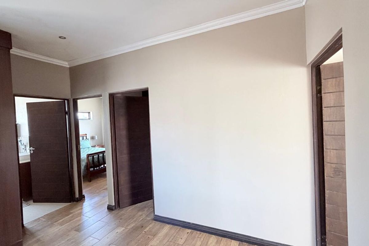 Spacious bedroom featuring modern wood-look tile flooring, built-in cupboards, and neutral wall finishes with elegant cove cornicing.