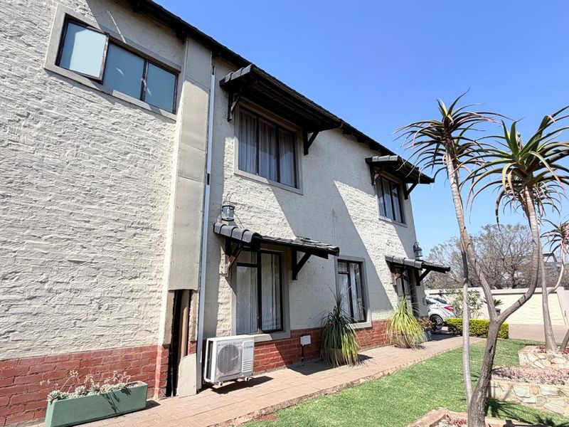 Rear elevation of a two-story brick house featuring a paved walkway, established garden, and external air conditioning unit.