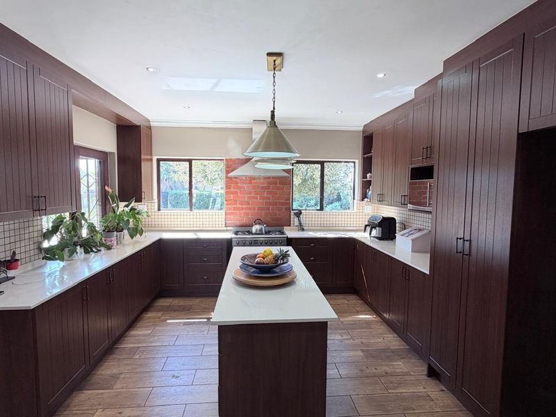Spacious kitchen featuring dark wood cabinetry, a central island with stone countertops, gas cooktop, and modern tiled flooring.