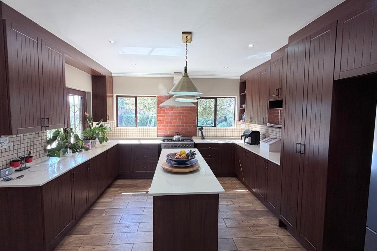 Spacious kitchen featuring dark wood cabinetry, a central island with stone countertops, gas cooktop, and modern tiled flooring.