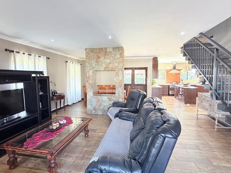 Spacious open-plan living area featuring a central stone-clad fireplace, tiled flooring, and a modern metal staircase leading to the upper level.