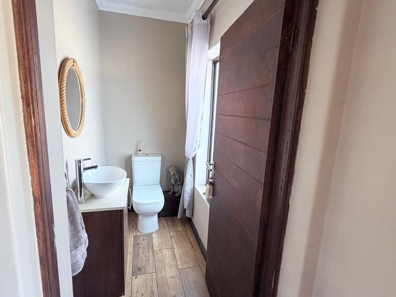 A compact guest bathroom featuring a modern vessel sink, vanity cabinet, and toilet with wood-look tiled flooring.