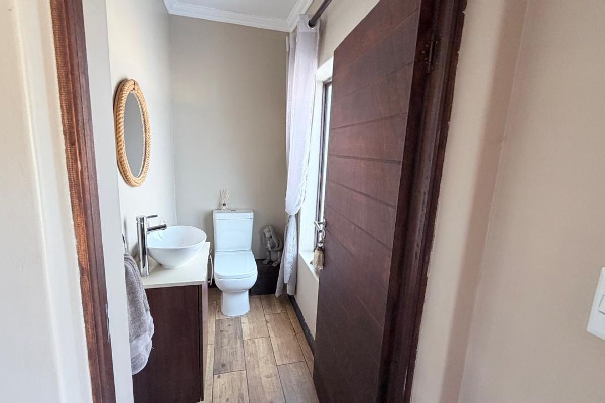 A compact guest bathroom featuring a modern vessel sink, vanity cabinet, and toilet with wood-look tiled flooring.