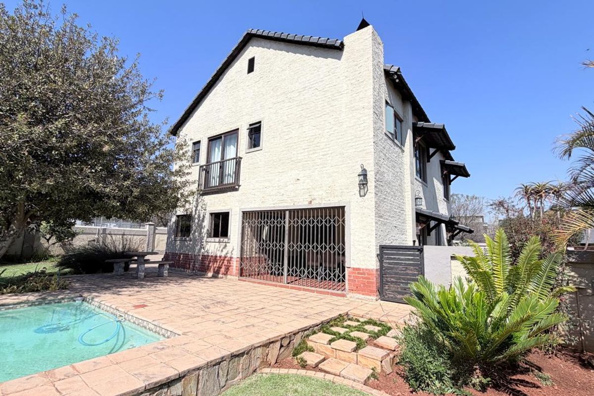 Rear exterior view of the house featuring a swimming pool, paved patio area, and a balcony overlooking the garden.