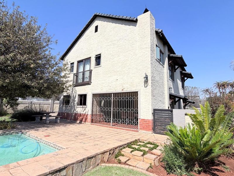 Rear exterior view of the house featuring a swimming pool, paved patio area, and a balcony overlooking the garden.