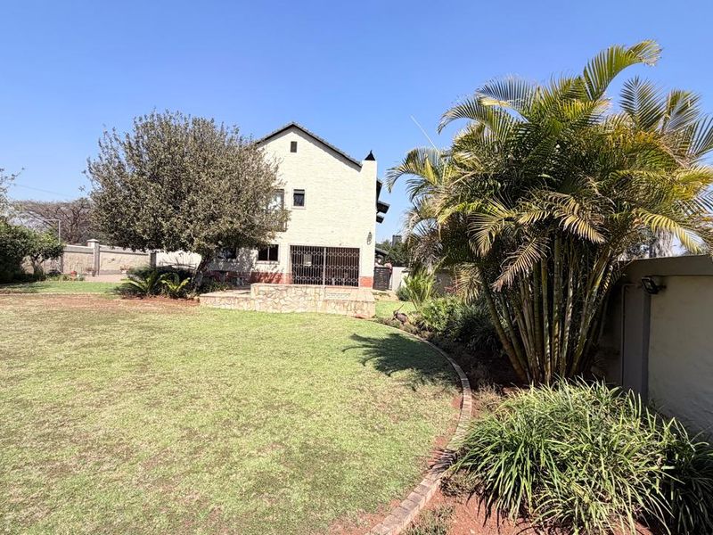 A spacious rear garden featuring a well-maintained lawn, mature palm trees, and a stone-clad patio area attached to the main house structure.
