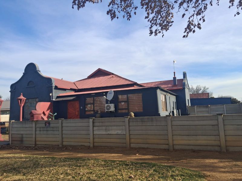 Front elevation of a house featuring a distinctive gabled roof, dark exterior paint, and a secure precast concrete boundary wall.