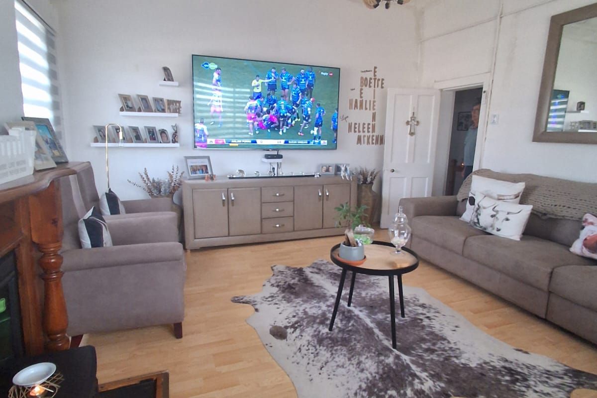 A comfortable living room featuring timber flooring, a decorative ceiling with a chandelier, and a fireplace, creating a warm and inviting atmosphere.