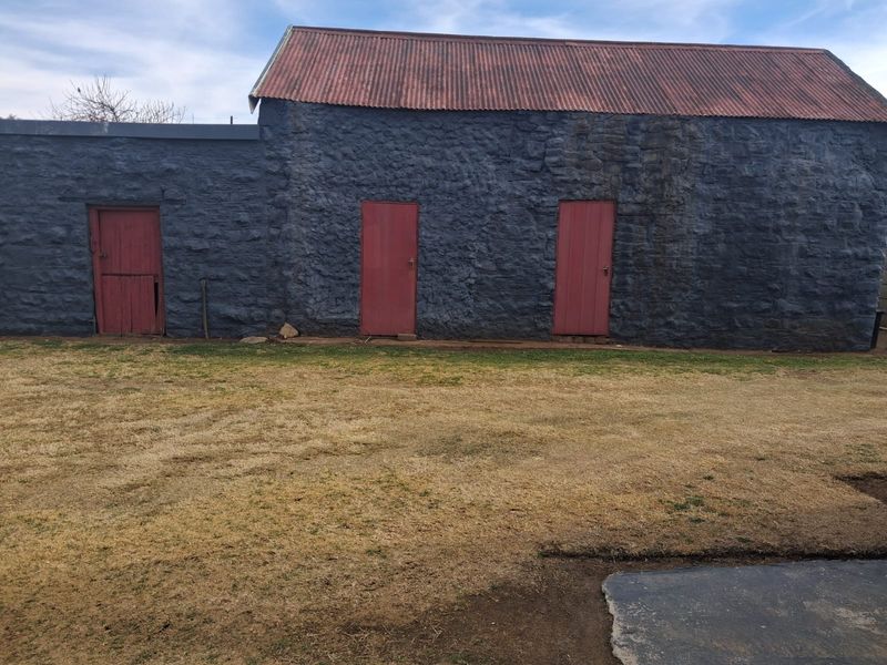 A rear view of a rustic stone outbuilding featuring a corrugated metal roof and three separate timber entrance doors.