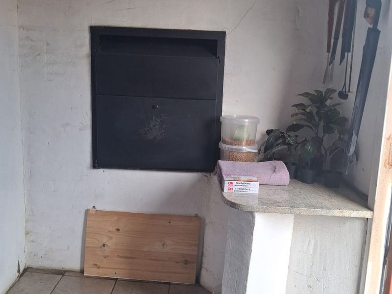 Covered patio area featuring a built-in braai, stone prep counter, and tiled flooring, requiring some cosmetic maintenance to the wall finishes.