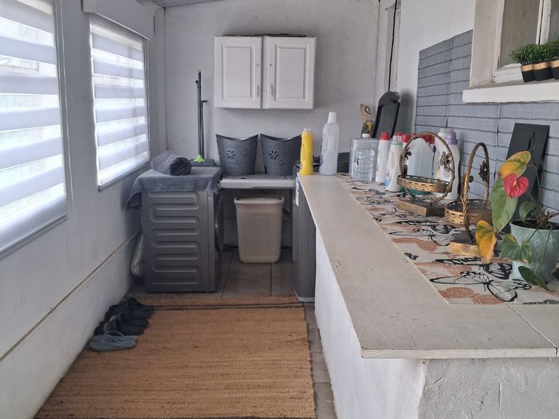 A functional laundry area featuring built-in cabinetry, a fixed countertop, tiled splashback, and roller blinds, providing a practical space for household utility tasks.