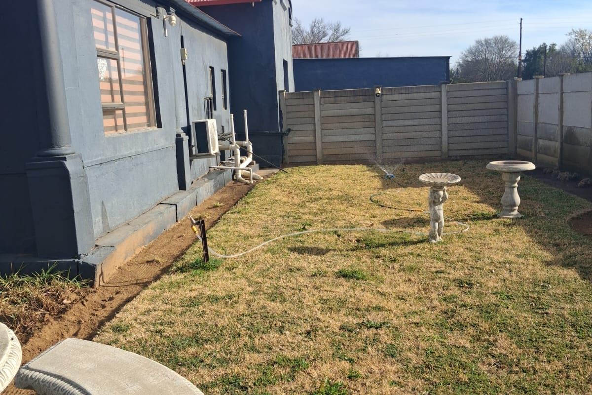 Rear garden area featuring a lawn, precast concrete boundary wall, and exterior building facade with an installed air conditioning unit.
