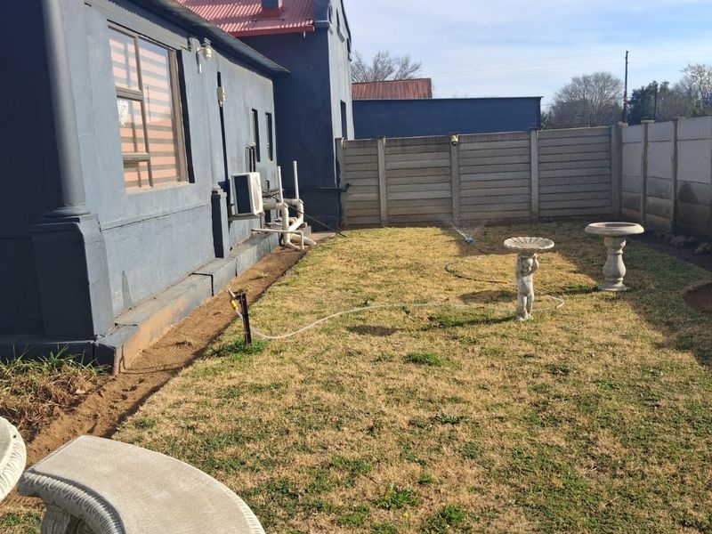 Rear garden area featuring a lawn, precast concrete boundary wall, and exterior building facade with an installed air conditioning unit.