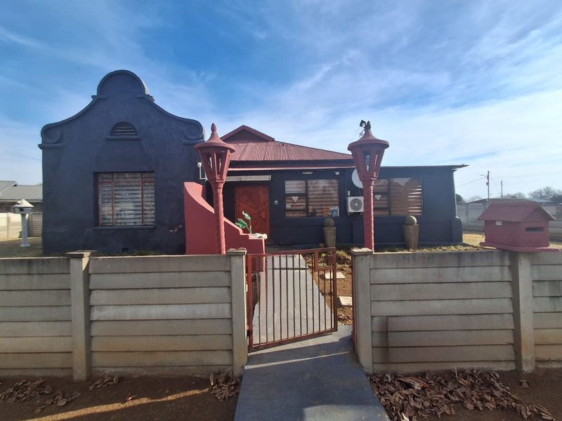 Front elevation of a house featuring a distinctive gable roof design, precast concrete boundary wall, and a gated pedestrian entrance.