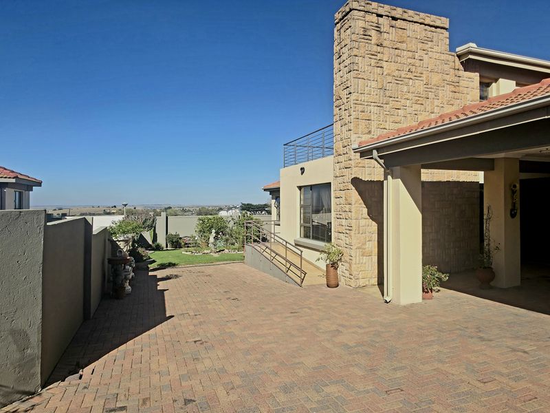 A spacious paved driveway leading to a covered carport, featuring a prominent stone-clad chimney and clear views of the surrounding landscape.