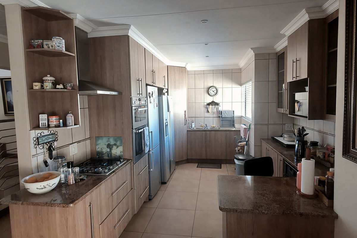 A functional kitchen featuring wood-finish cabinetry, granite countertops, built-in oven, gas hob, and tiled flooring, with an adjacent staircase.