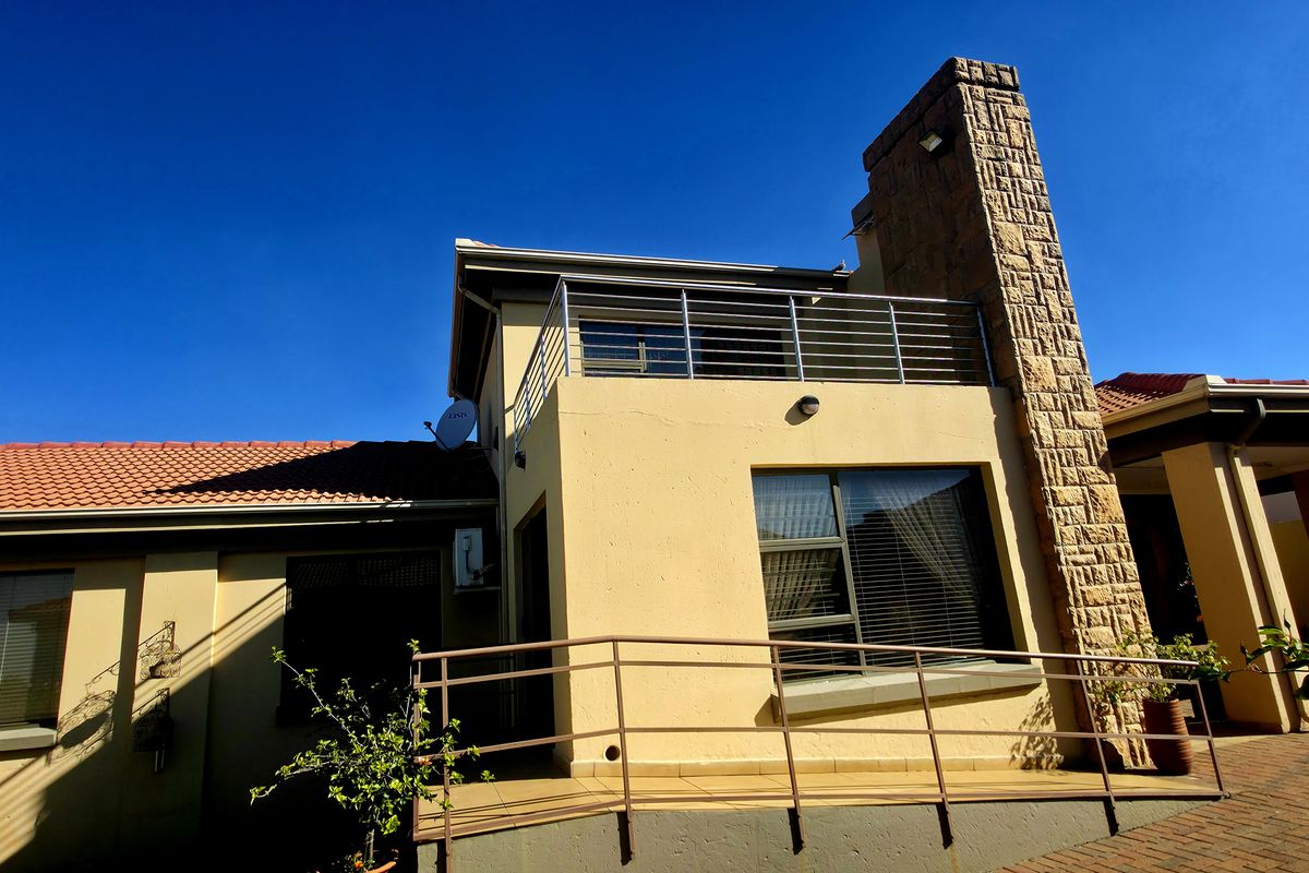 Rear view of the property featuring a stone-clad chimney, a balcony with metal railings, and a paved patio area with a wheelchair access ramp.
