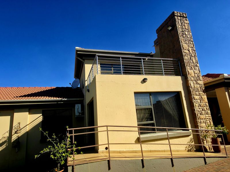 Rear view of the property featuring a stone-clad chimney, a balcony with metal railings, and a paved patio area with a wheelchair access ramp.