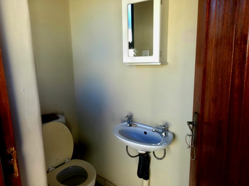 A compact guest bathroom featuring a wall-mounted basin, toilet, and medicine cabinet, finished with a solid timber door.