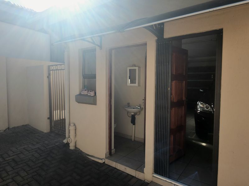A paved rear courtyard area featuring an external washbasin, security gate, and access to the garage via a sliding security door.