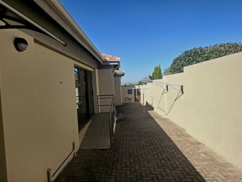 A paved side passage or rear exterior area featuring a ramp, boundary wall, and wall-mounted clothesline.