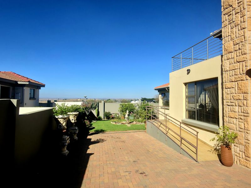 A well-maintained rear courtyard featuring brick paving, stone-clad exterior walls, a metal balustrade, and a ramp leading to the property entrance.