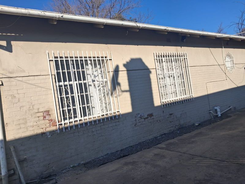 Rear exterior view of the property showing brick walls with security bars on windows and concrete paving.
