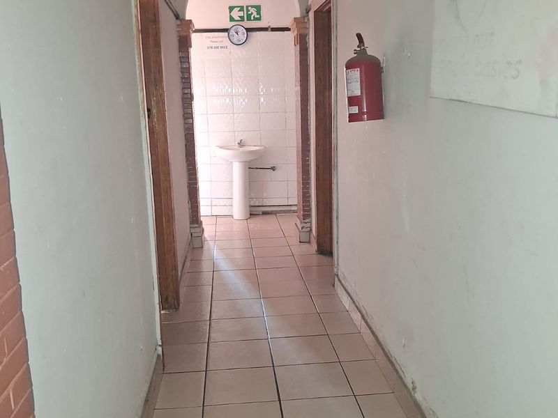 A functional hallway featuring tiled flooring, an arched transition, and a pedestal basin at the end, showing signs of wear and tear.