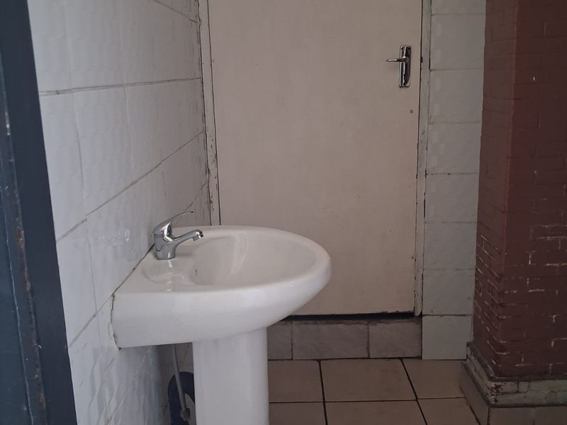A small bathroom or wash area featuring a pedestal basin, tiled flooring, and tiled walls, currently in need of cosmetic updates.