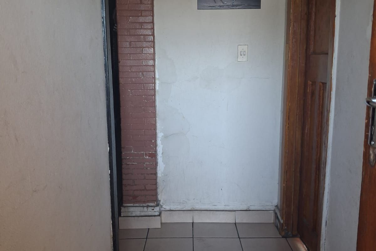 A narrow hallway featuring tiled flooring, a decorative brick pillar, and wooden door frames, showing signs of wear and requiring cosmetic attention.