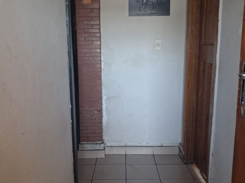 A narrow hallway featuring tiled flooring, a decorative brick pillar, and wooden door frames, showing signs of wear and requiring cosmetic attention.