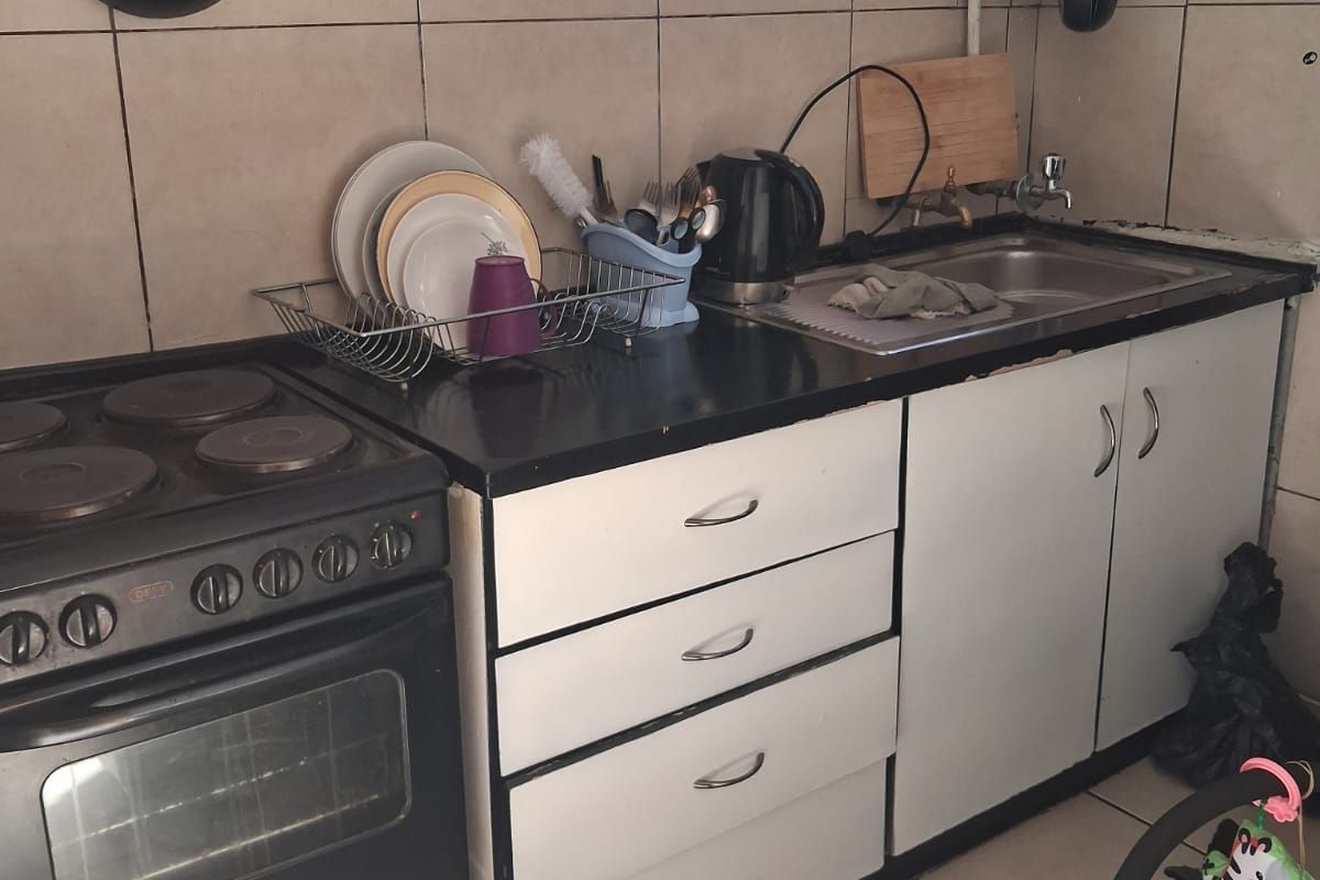 A compact kitchen featuring tiled flooring, a tiled backsplash, built-in cabinetry, and an electric stove, showing signs of wear and wall damage.