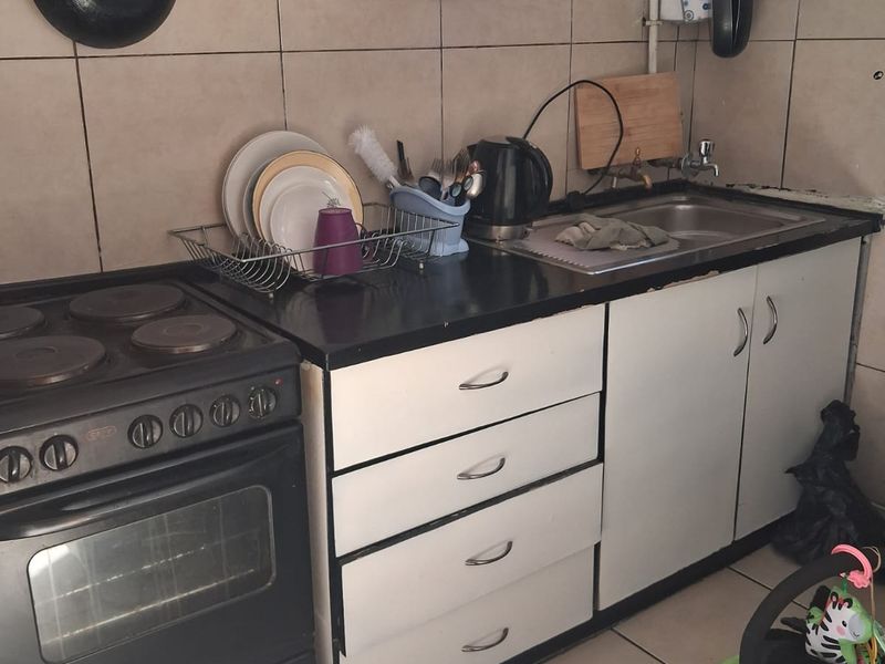 A compact kitchen featuring tiled flooring, a tiled backsplash, built-in cabinetry, and an electric stove, showing signs of wear and wall damage.