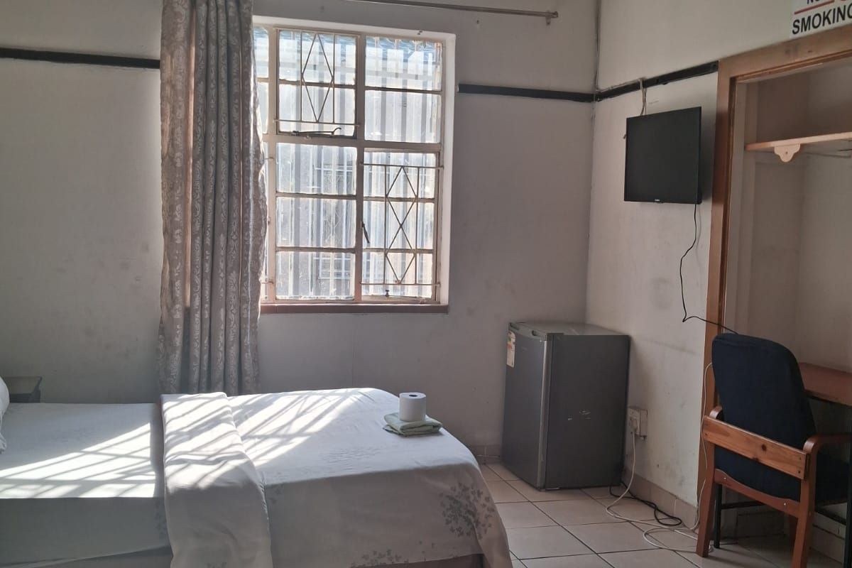 A bedroom featuring tiled flooring, a decorative pressed metal ceiling, and a built-in alcove, currently showing signs of wear and ceiling water damage.
