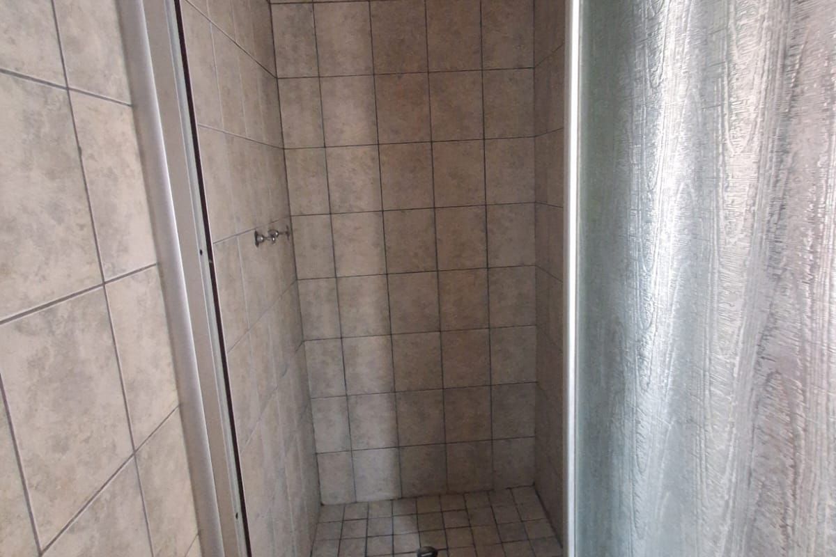 A functional shower stall featuring tiled walls and flooring with a glass enclosure, requiring minor maintenance and cosmetic updates.