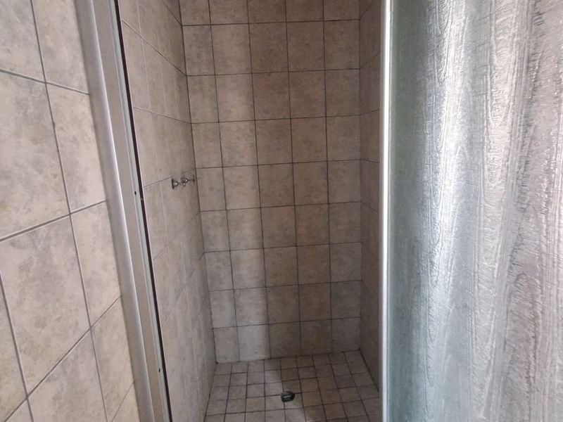 A functional shower stall featuring tiled walls and flooring with a glass enclosure, requiring minor maintenance and cosmetic updates.