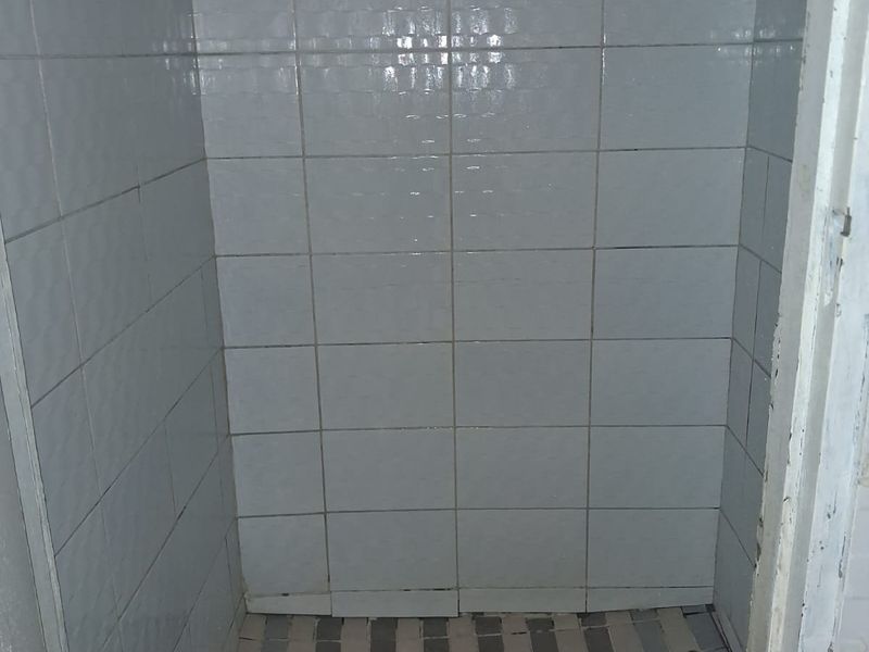 A small shower enclosure featuring white wall tiles and a damaged tiled floor, requiring maintenance or renovation.