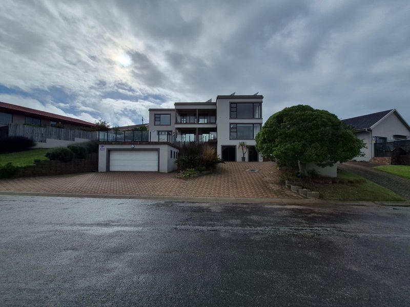 A modern multi-story residential property featuring a paved driveway, integrated garage, and multiple balconies with large windows.