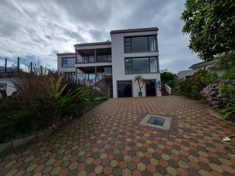 A modern multi-level residential property featuring a paved driveway, glass balustrades, and large windows, presenting a clean and well-maintained exterior facade.