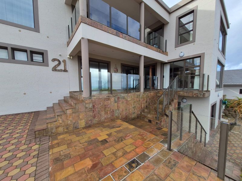 A modern multi-level home entrance featuring stone-clad stairs, glass balustrades, and a paved patio area with sliding door access.