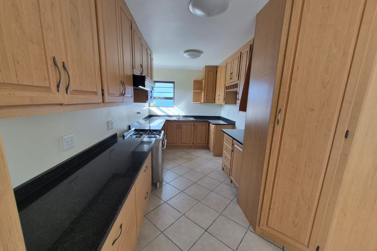 A functional kitchen featuring light wood cabinetry, dark granite countertops, a gas stove, and tiled flooring, offering ample storage and workspace.