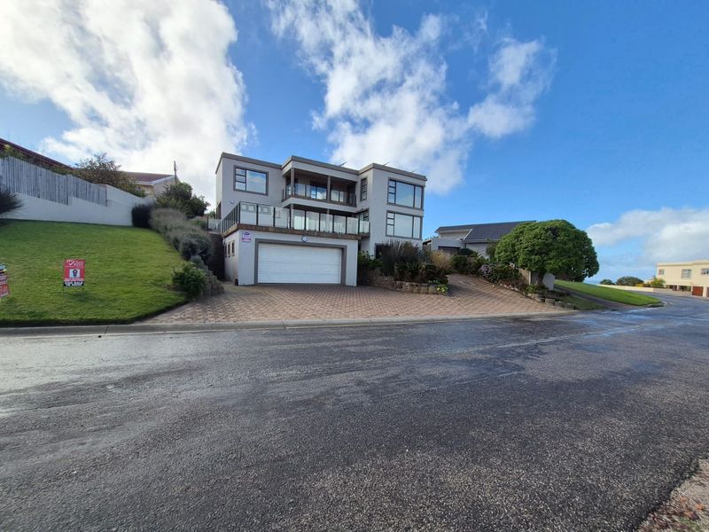 Modern multi-story residential property featuring a double garage, paved driveway, and elevated balconies with glass balustrades.