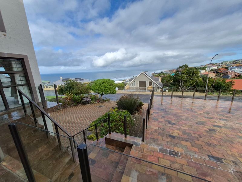 Elevated outdoor terrace featuring stone paving and glass balustrades, offering expansive coastal and neighbourhood views.