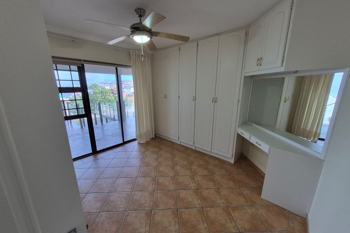Spacious bedroom featuring built-in cupboards, a vanity, tiled flooring, and a ceiling fan, with direct access to an outdoor balcony.