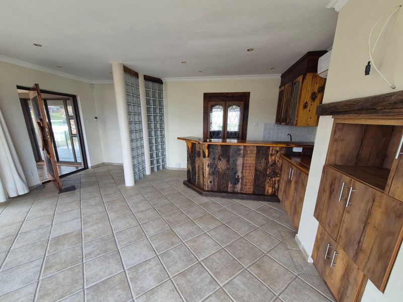 An open-plan bar area featuring rustic wooden cabinetry, a built-in bar counter, glass block feature wall, and tiled flooring with direct patio access.